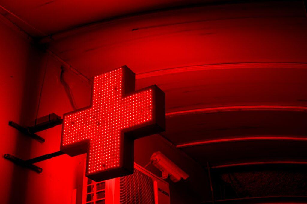 A glowing red illuminated cross sign mounted on a wall, casting intense red light across the surrounding ceiling and surfaces.