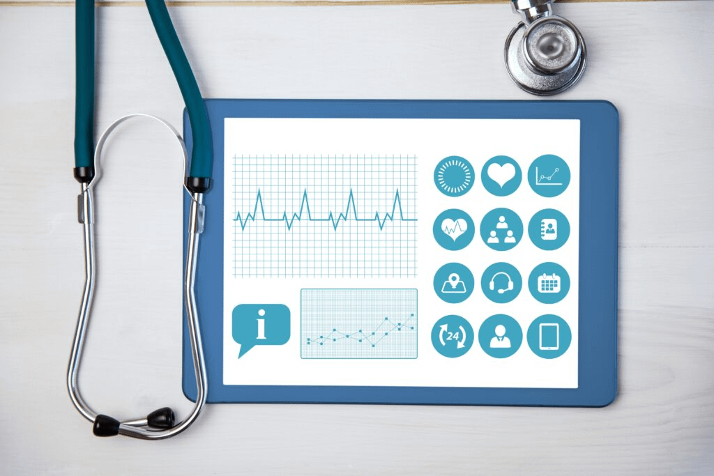 Digital tablet displaying medical charts and health icons on a desk beside a stethoscope.